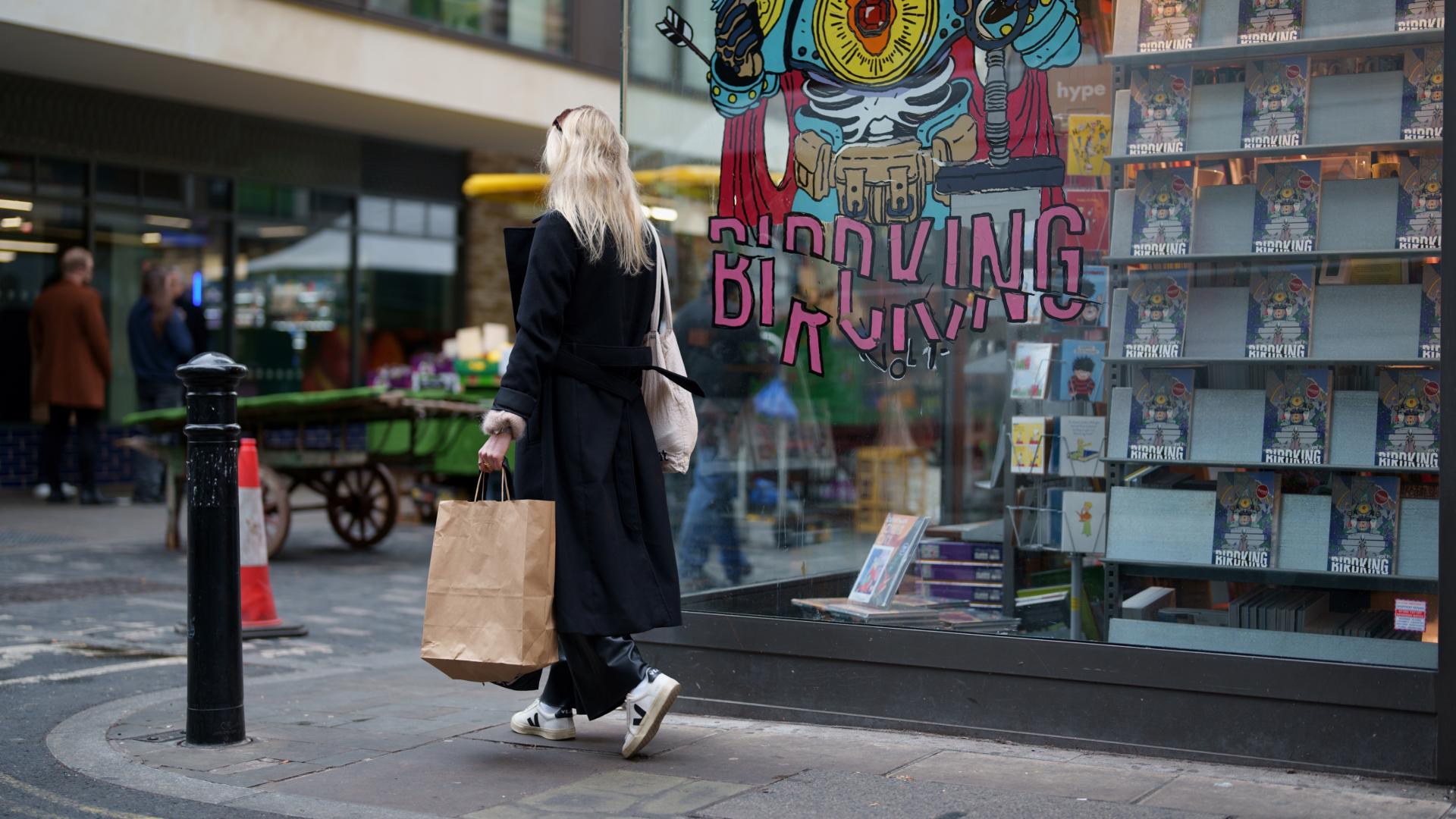 A photo of a woman holding a shopping bag whilst walking outside the high street.
