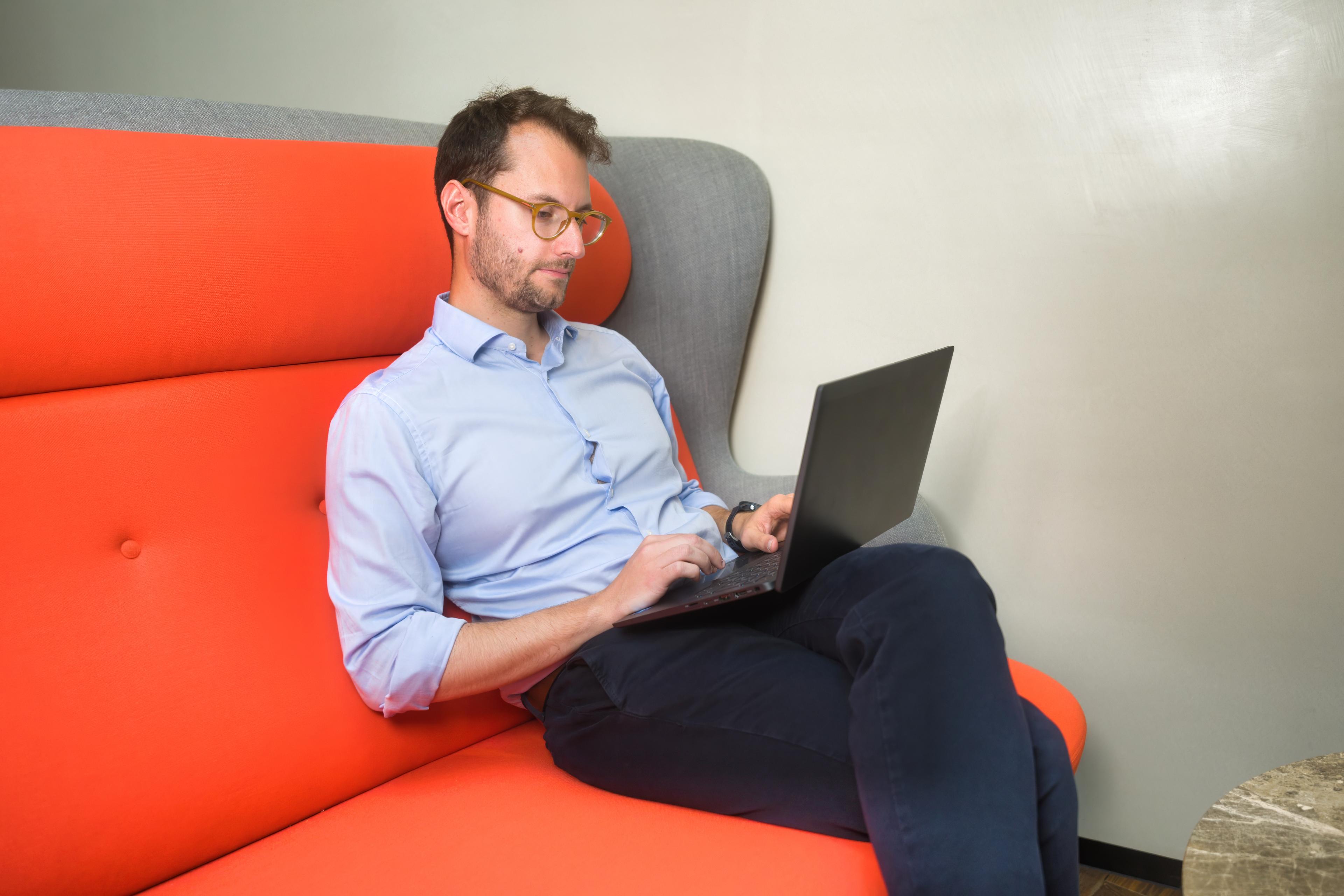A photo of a Trustpilot employee sat on an office couch and working on his laptop
