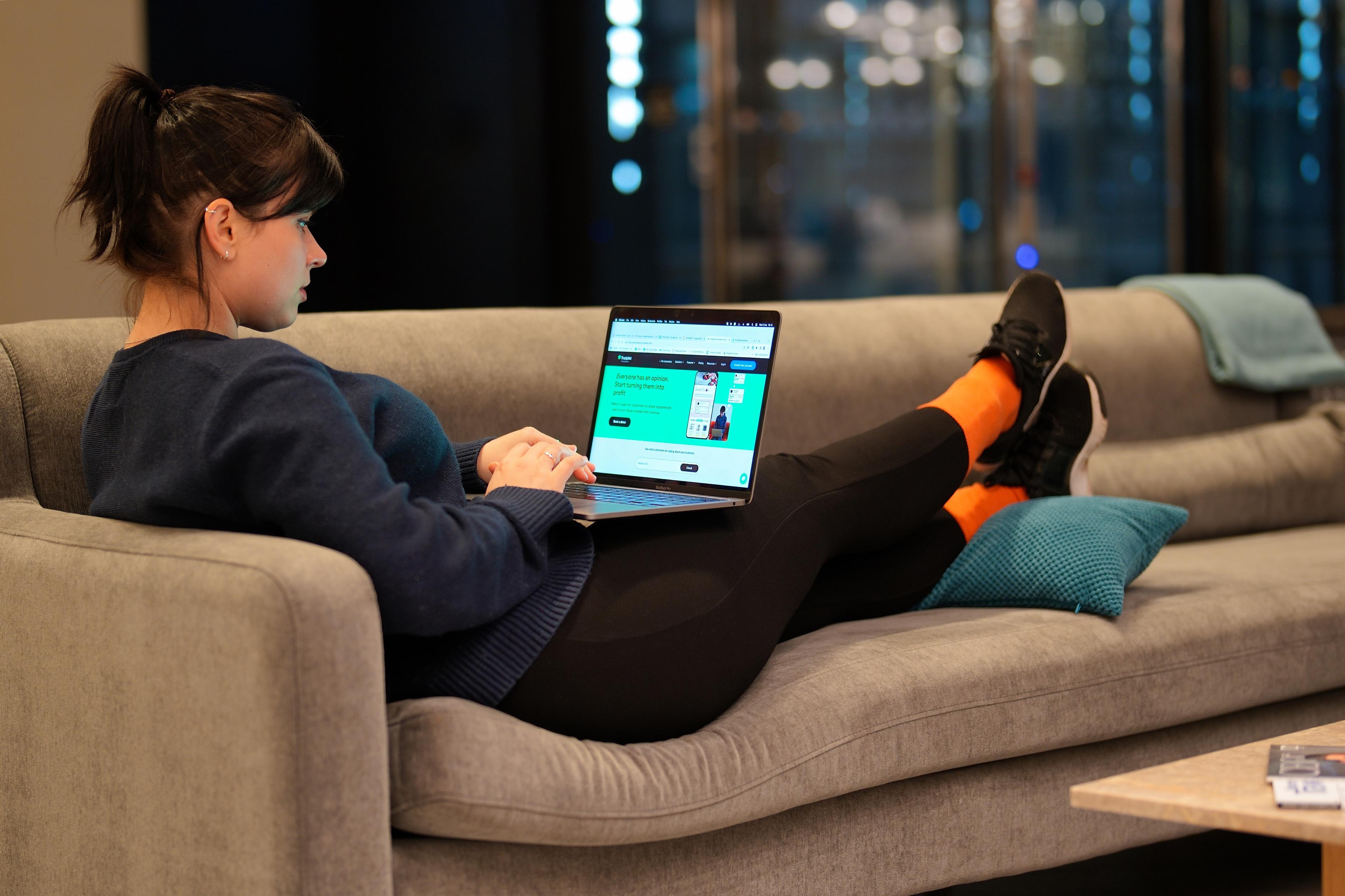 A photo of a Trustpilot employee working on her laptop, with her feet up on the couch